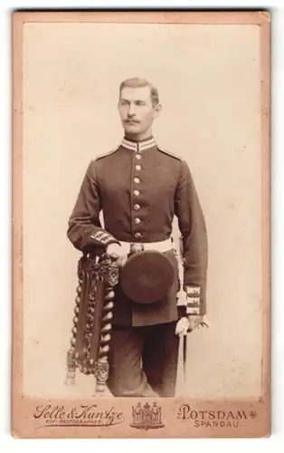 Fotografie Selle & Kuntze, Potsdam, Portrait Soldat in Uniform mit Schirmmütze am Stuhl lehnend