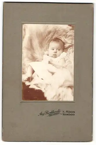 Fotografie Aug. Burkhardt, Neumünden, Portrait niedliches Kleinkind im weissen Kleid auf Fell sitzend