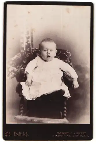 Fotografie Ph. Helfrich, New York, Portrait niedliches Kleinkind im weissen Kleid auf Stuhl sitzend