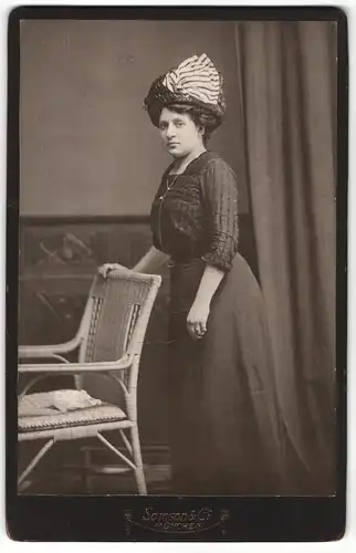 Fotografie Samson & Co., München, Portrait bürgerliche Dame mit Hut an Stuhl gelehnt