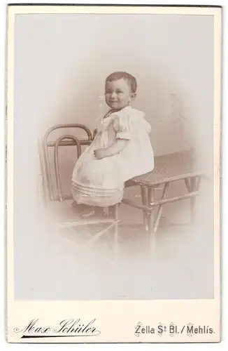 Fotografie Max Schüler, Zella St. Bl. / Mehlis, Portrait kleines Mädchen im weissen Kleid auf Tisch sitzend