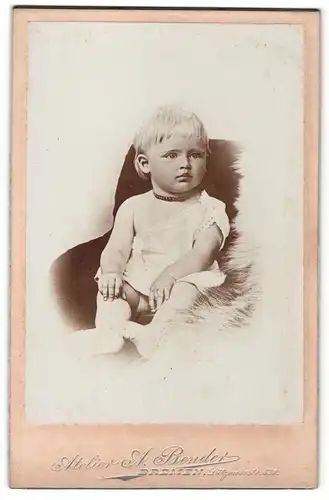 Fotografie A. Bender, Bremen, Portrait sitzendes Kleinkind im weissen Hemd mit nackigen Füssen