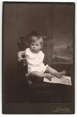 Fotografie Max Voigt, Zwickau, Portrait sitzendes Kleinkind im weissen Hemd mit nackigen Füssen und Zeitung