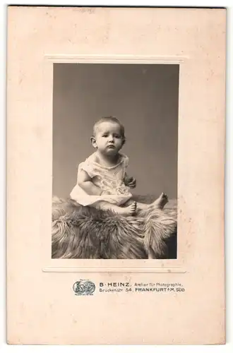 Fotografie B. Heinz, Frankfurt a / M., Portrait süsses Kleinkind im weissen Hemd auf Fell sitzend