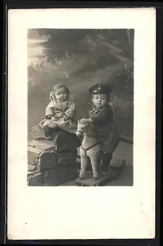 Foto-AK Knabe in Uniform auf Spielzeugpferd, Süsse Schwester auf Mauerrest