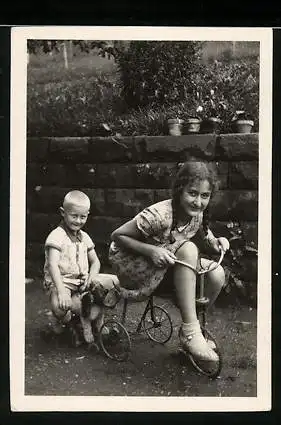 Fotografie Mädchen fährt auf kleinem Dreirad, Knabe auf Spielzeug-Hund sitzend