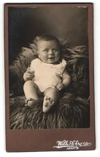 Fotografie Wilh. Schroers, Lehrte, Portrait süsses Kleinkind im weissen Hemd auf Fell sitzend