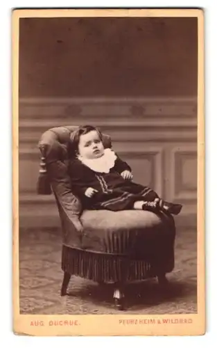 Fotografie Aug. Ducrue, Pforzheim, Portrait sitzendes Kleinkind im hübschen Kleid mit Latz