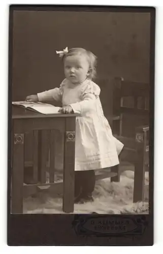 Fotografie G. Klimmer, Bückeburg, Portrait blondes niedliches Mädchen mit Kinderbuch am Tisch