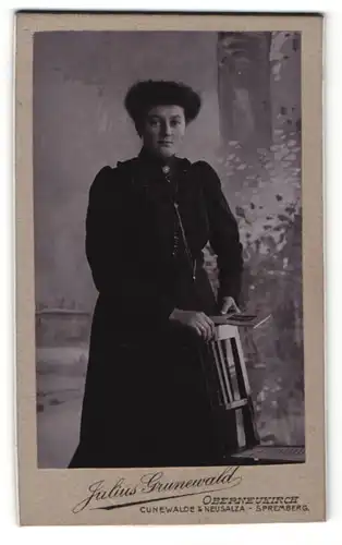 Fotografie Julius Grunewald, Oberneukirch, Portrait dunkelhaarige Schönheit im Kleid am Stuhl stehend