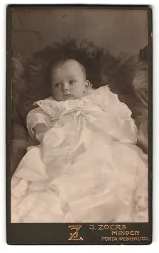 Fotografie J. Zerb, Minden, Portrait süsses Baby im weissen Kleid auf Fell sitzend