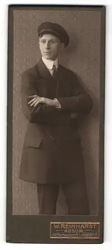 Fotografie W. Reinhardt, Husum, Portrait modisch gekleideter Herr mit Schirmmütze und verschränkten Armen