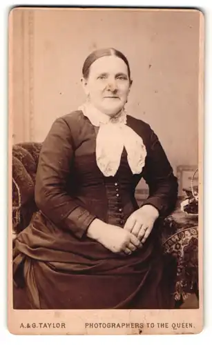 Fotografie A. & G. Taylor, Stockton, Portrait ältere Dame in hübscher Kleidung am Tisch sitzend
