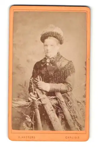 Fotografie H. Andrews, Carlisle, Portrait hübsch gekleidete Dame mit Hut an Zaun gelehnt