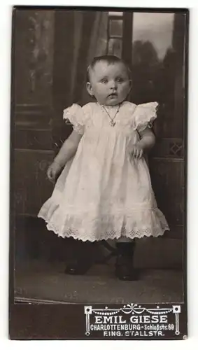 Fotografie Emil Giese, Berlin-Charlottenburg, Portrait niedliches Kleinkind im weissen Kleid mit Herzkette
