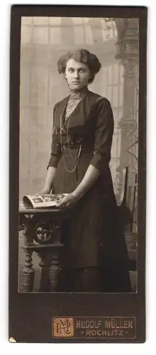 Fotografie Rudolf Müller, Rochlitz, Junge Dame in langem schwarzen Kleid mit Fotoalbum und langer Kette