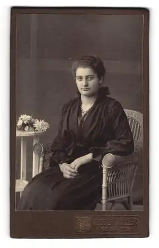 Fotografie Rudolf Müller, Rochlitz, Junge Dame in schwarzem Kleid sitzend auf Korbstuhl mit Halskette
