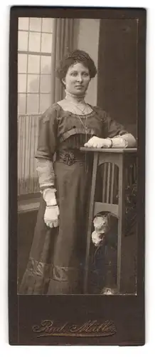 Fotografie Rud. Müller, Ort unbekannt, Hübsche junge Frau in dunklem Kleid mit Handschuhen und langer Kette
