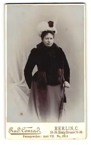 Fotografie Rud. Conrad, Berlin, Dame im dunklen Kleid mit Pelzschal und Federhut samt Schirm