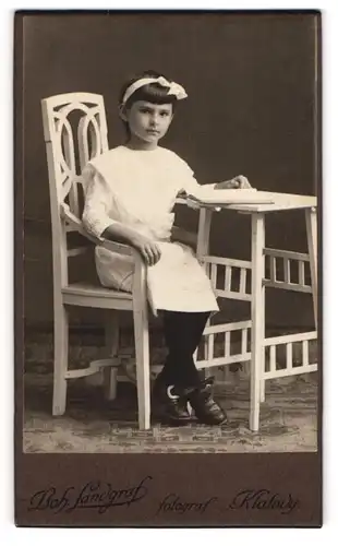 Fotografie Boh. Landgraf, Klatovy, junges Mädchen im weissen Kleid sitzend am Tisch mit Schulbuch