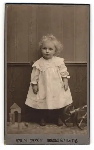 Fotografie Willy Dose, Bremen, niedliches Mädchen im weissen Kleid mit Spielzeugkanone und Bauklötzen