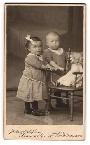Fotografie Samson & Co., Halle / Saale, zwei niedliche Kinder mit ihrer Puppe auf dem Stuhl