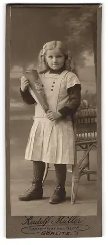 Fotografie Rudolf Müller, Görlitz, Mädchen im Hauskleid mit Zuckertüte zur Einschulung