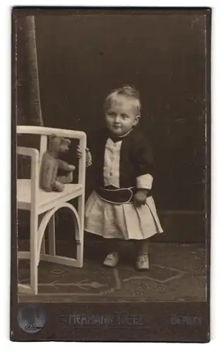 Fotografie Hermann Tietz, Berlin, niedliches Kind im Kleid mit Teddybär auf dem Stuhl