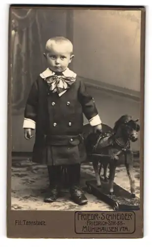 Fotografie Friedr. Schneider, Mühlhausen i. th., junges Kind im Winterkleid mit Schaukelpferd auf Rädern