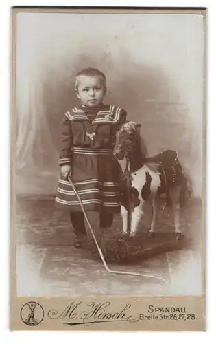 Fotografie M. Hirsch, Spandau, kleines Kind mit geflecktem Schaukelpferd auf Rädern im Atelier