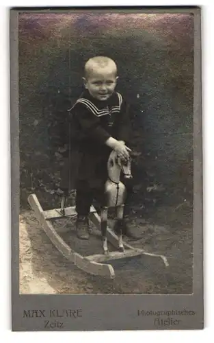 Fotografie Max Klare, Zeitz, kleiner Knabe im dunklen Kleid auf seinem Schaukelpferd