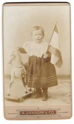 Fotografie A. Jandorf & Co., Berlin, kleines Mädchen mit Schaukelpferd auf Rädern und Flagge in der Hand