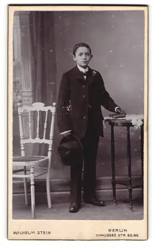 Fotografie Wilhelm Stein, Berlin, junger Knabe im Anzug mit Hut und Bibel zur Kommunion
