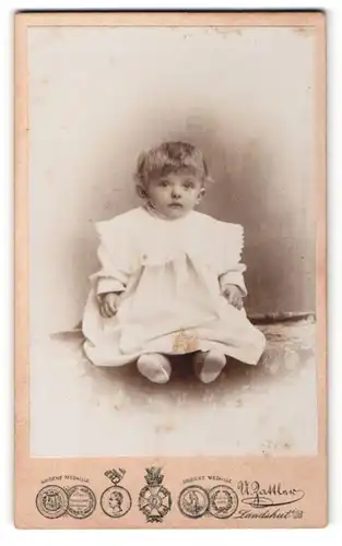 Fotografie U. Zattler, Landshut, Portrait niedliches Kleinkind im weissen Kleid auf Tisch sitzend