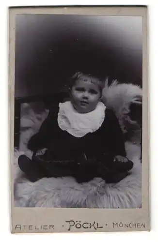 Fotografie Atelier Pöckl, München, Portrait Kind posiert sitzend auf einem weissen Fell