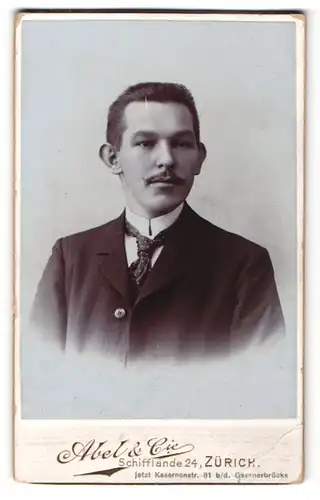 Fotografie Abel & Cie, Zürich, Portrait charmanter Herr im Anzug mit Krawatte und Zwirbelbart