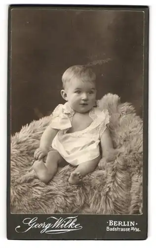 Fotografie Georg Wilke, Berlin, Badstrasse 35 /36, Süsses Kleinkind im weissen Kleidchen auf einem Fell sitzend