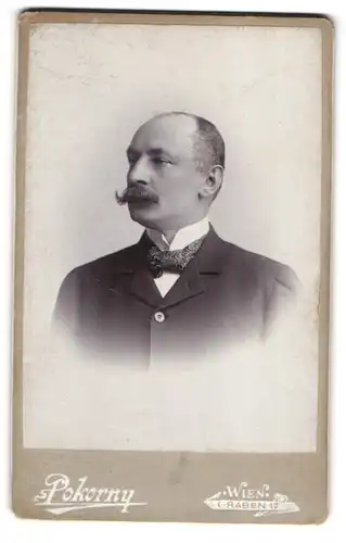 Fotografie Pokorny, Wien, Graben 17, Junger Herr in schwarzem Anzug mit gezwirbelten Schnurrbart und gemusteter Krawatte