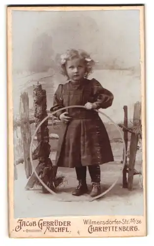 Fotografie Jacob Gebrüder, Charlottenburg, Wilmersdorfer Str. 55, Niedliches Mädchen in schwarzem Kleid mit Reifen