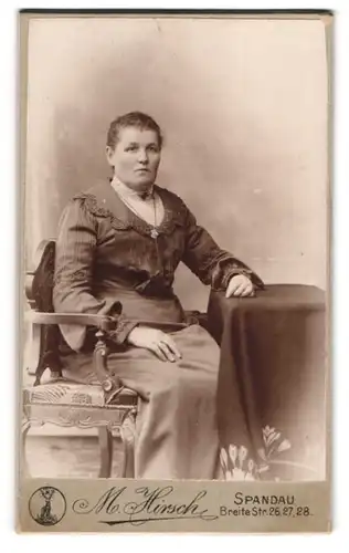 Fotografie M. Hirsch, Spandau, Breite Str. 26, Bürgerliche Dame in Kleid mit Kette und dunklen Haaren am Tisch sitzend