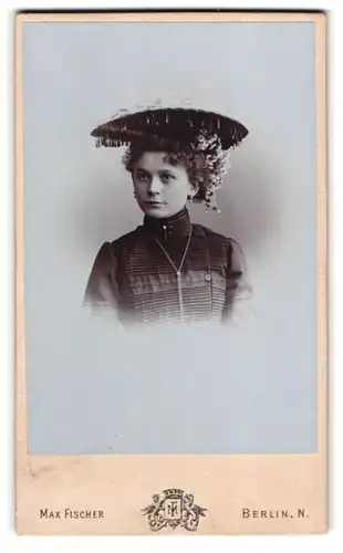 Fotografie Max Fischer, Berlin, Danziger Str. 98, Hübsche junge Dame in schwarzem Kleid mit Hut und Blumenschmuck
