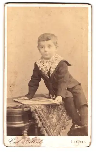 Fotografie Carl Bellach, Leipzig, Gellertstr. 12, Niedlicher Junge in schwarzem Matrosenhemd mit Bilderbruch