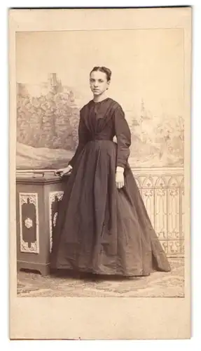 Fotografie C. Leupold, Heidelberg, hübsche junge Frau im dunklen Kleid vor einer Studiokulisse