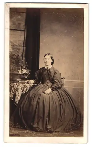 Fotografie R. Griffiths C. A. M., Truro, junge Frau im weiten dunklem Kleid posiert sitzend am Tisch