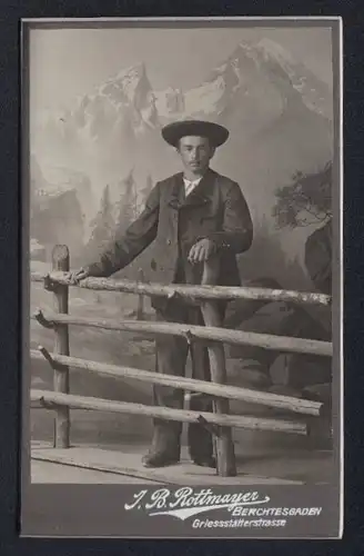 Fotografie J. B. Rottmayer, Berchtesgaden, junger Bayer im Anzug hinter einem Zaun, Studiokulisse