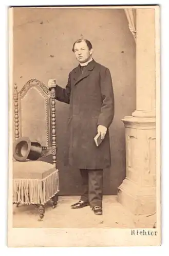 Fotografie J. G. Richter, Budweis, junger Pastor im Mantel mit Zylinder auf dem Sessel
