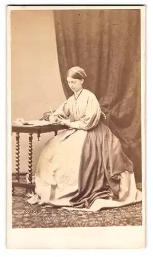 Fotografie unbekannter Fotograf und Ort, junge Frau im hellen Kleid schreibt einen Brief am Tisch