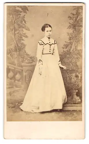 Fotografie Mr. & Mrs. Ward, London, junge Engländerin im weissen Kleid posiert vor einer Studiokulisse