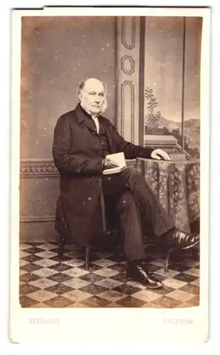 Fotografie Reynolds, Padstow, älterer Herr im Anzug mit aufgeschlagenem Buch vor einer Studiokulisse