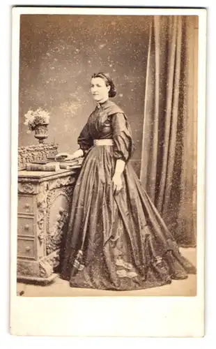 Fotografie Medcalfe & Evans, Tenby, junge Waliserin im dunklen Kleid stehend an einer Kommode